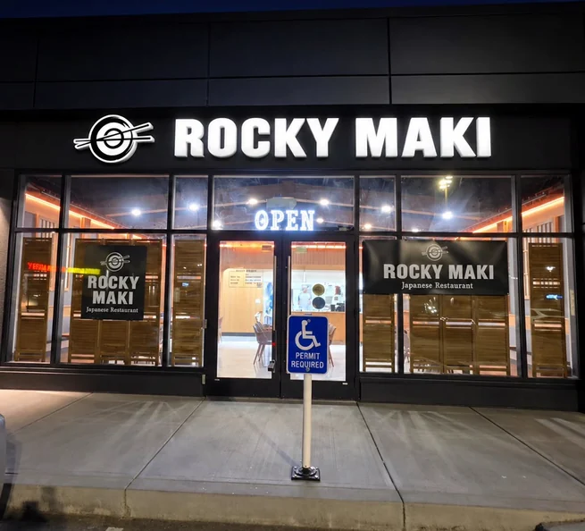 Rocky Maki storefront at night with its lit sign and open door in West Springs, Calgary