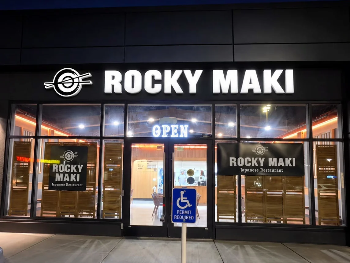 Rocky Maki storefront at night with its lit sign and open door in West Springs, Calgary